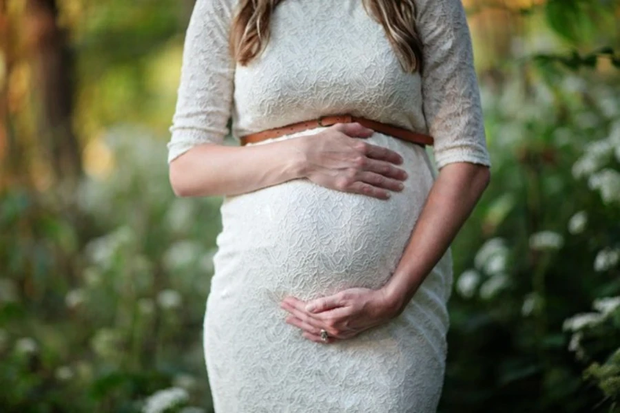 Una mujer embarazada con un vestido de maternidad de encaje que enmarca la figura.