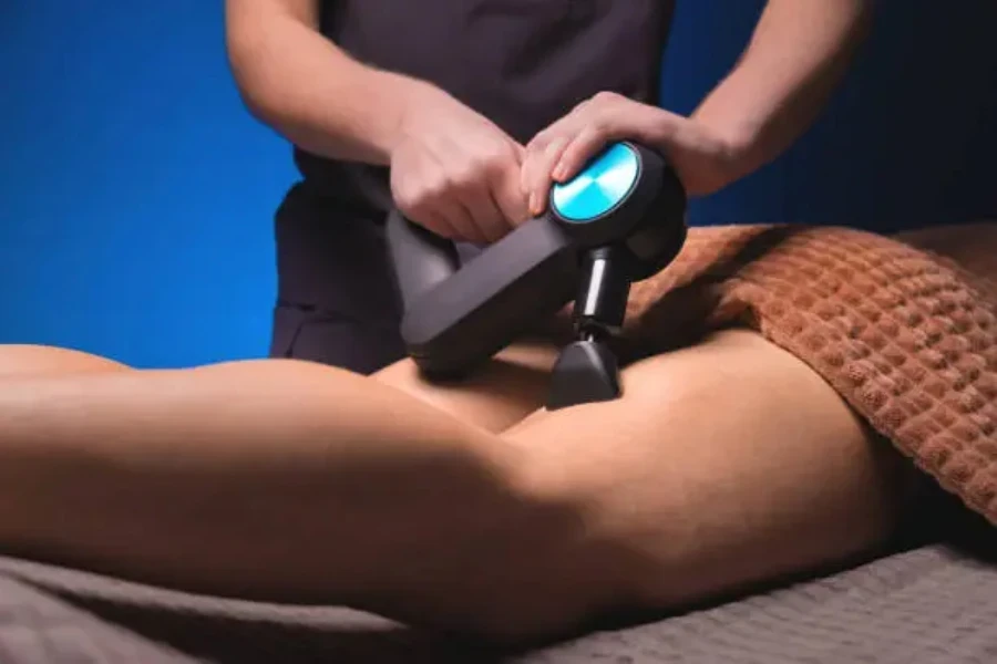 Man using massage gun on leg of patient