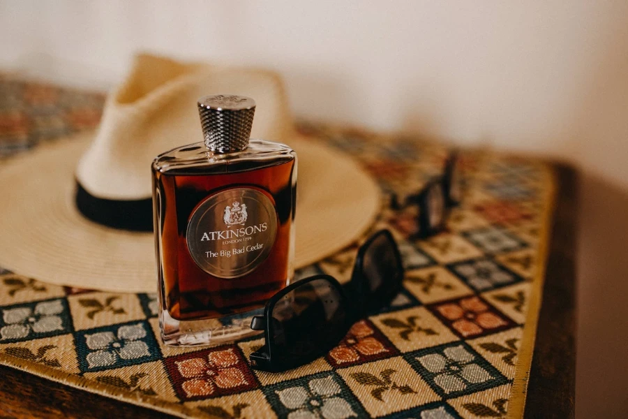 Cologne bottle on a table beside a man's hat and sunglasses