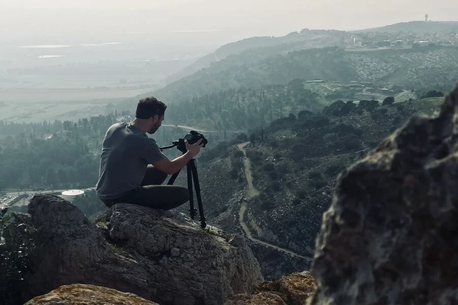 Uomo seduto su una roccia mentre usa la fotocamera montata su un supporto