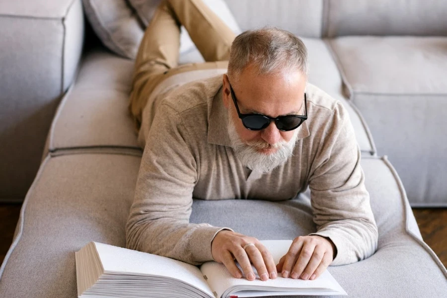 Homme plus âgé, allongé sur un canapé, lisant un livre en braille