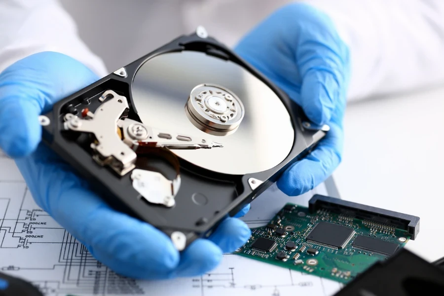 Teknisi dengan sarung tangan biru memegang hard disk drive