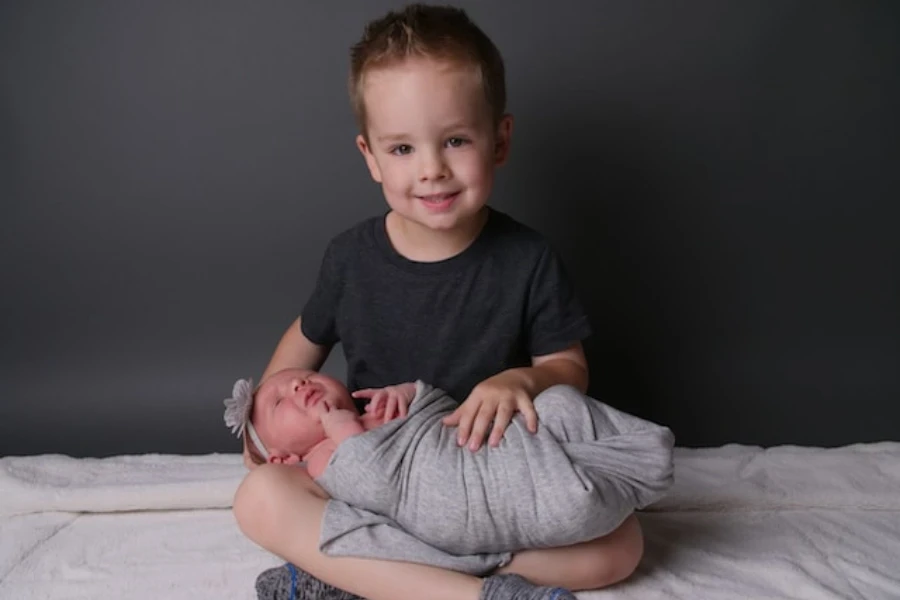 A boy holding a baby in a gray swaddle