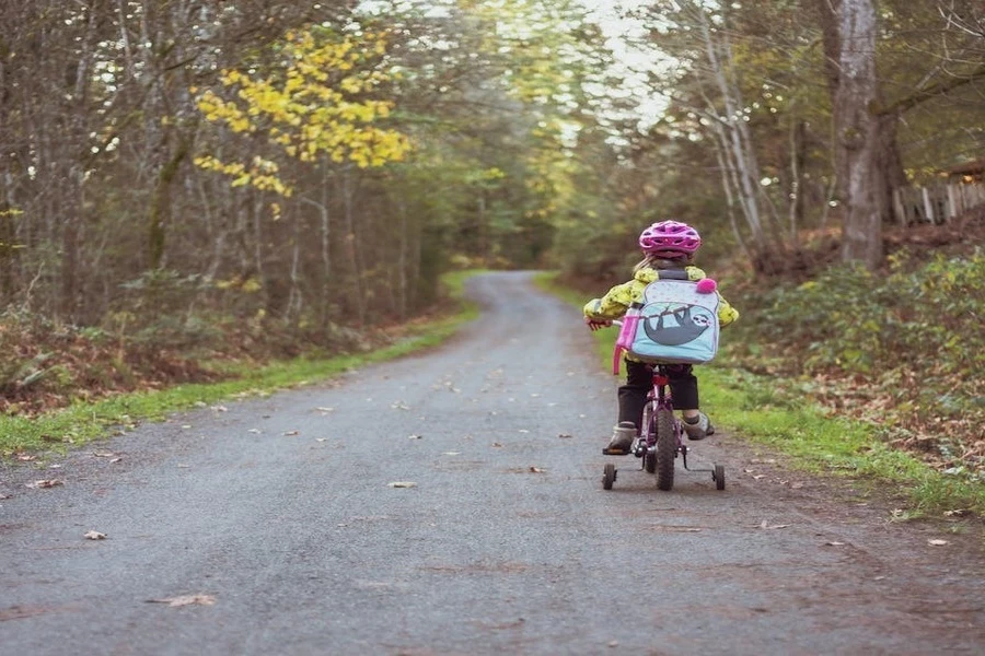 Un niño andando en bicicleta con una bolsa y un casco.