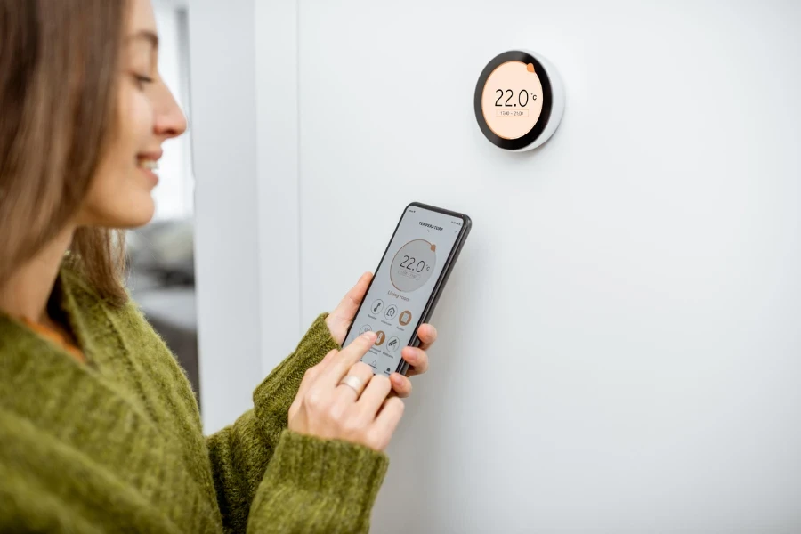 Person, die mit ihrem Telefon einen intelligenten Thermostat steuert