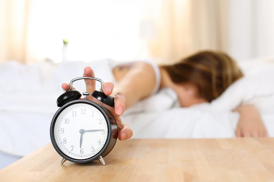 woman in bed reaching to alarm clock