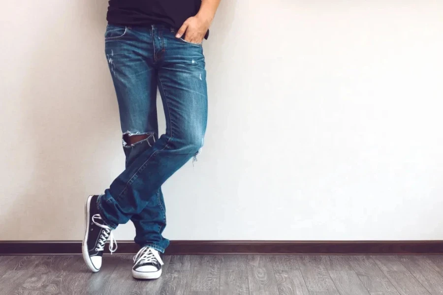 young fashion man's legs in jeans and sneakers on wooden floor