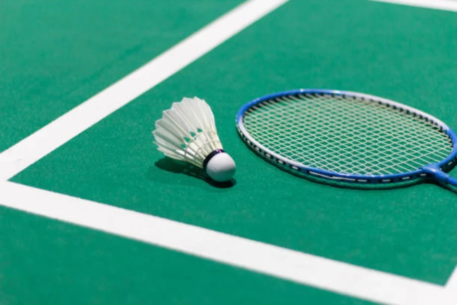 Feather shuttlecock sitting on court next to badminton racquet