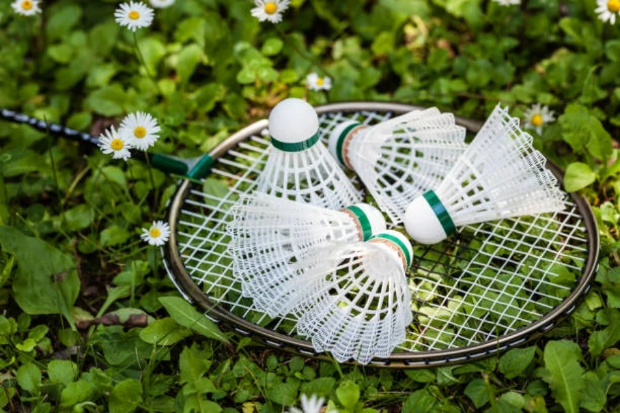 Fünf weiße Badminton-Federbälle aus Kunststoff sitzen auf einem Schläger im Gras