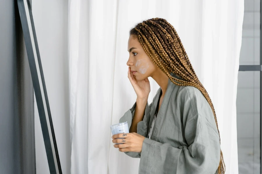 Personne avec de longues tresses appliquant une crème hydratante sur son visage