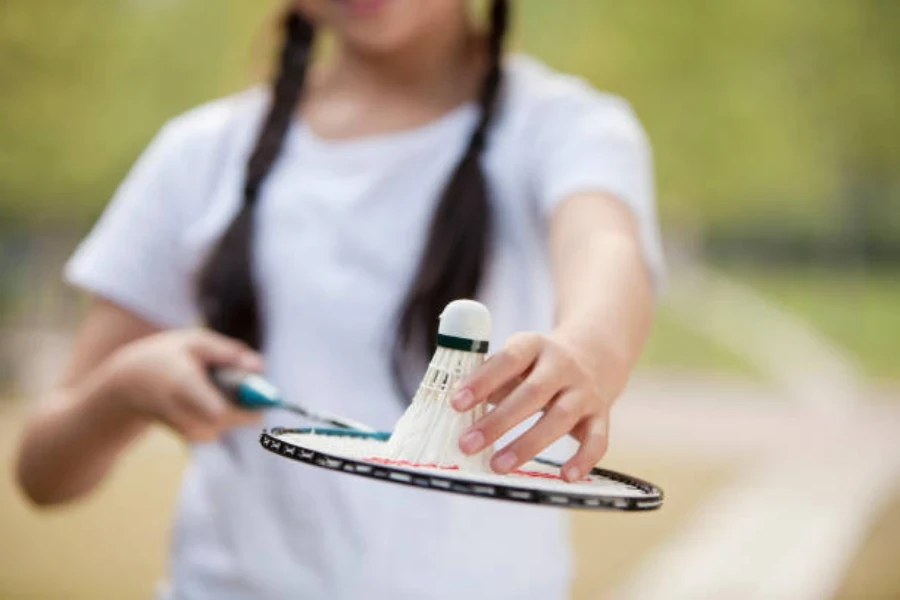 Üstünde tüylü raketle olan bir badminton raketi tutan kadın