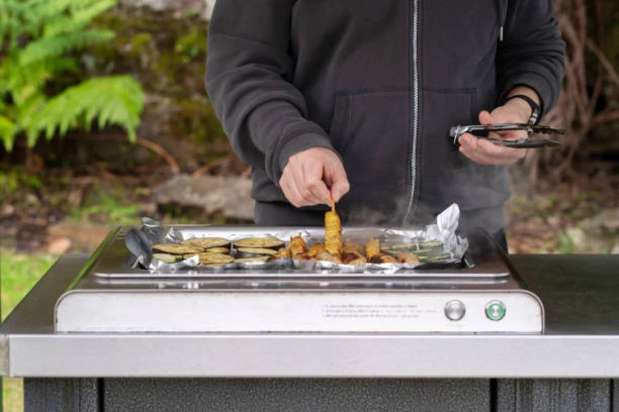 Mann benutzt Elektrogrill im Freien, um Gemüse und Hühnchen zu kochen