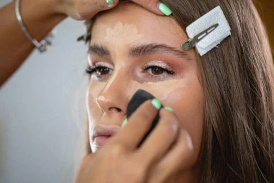 Una esteticista aplicando base en el rostro de una mujer usando una esponja de maquillaje.