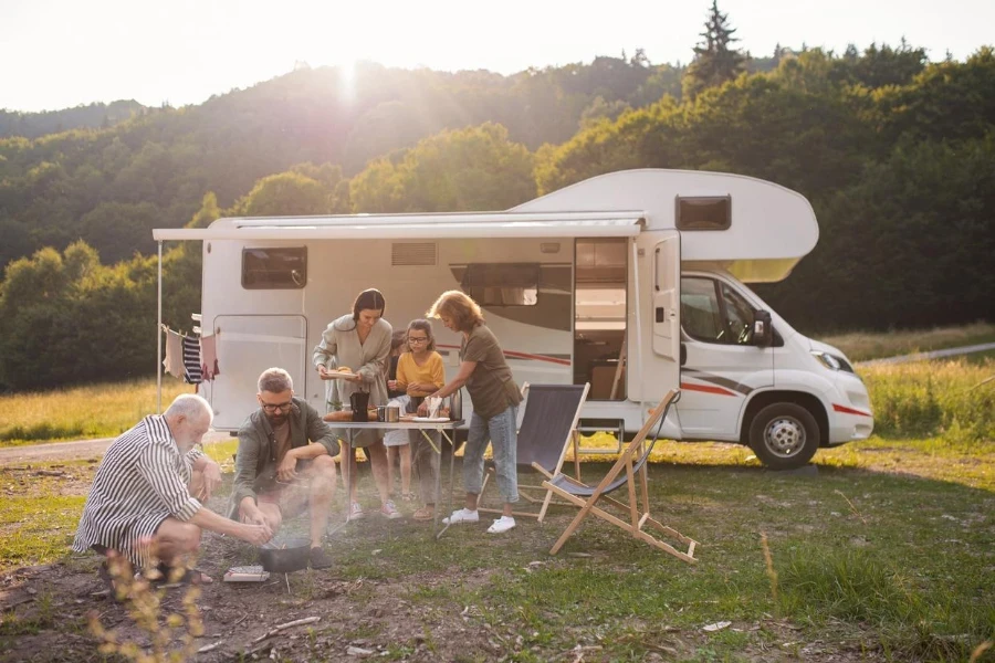 Eine Familie sitzt und isst draußen neben einem Wohnwagen