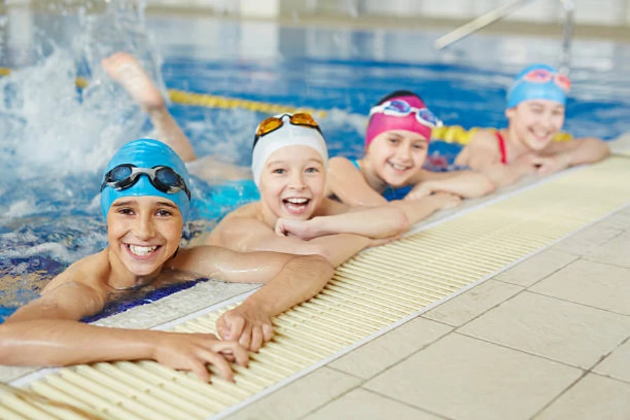 Children lined up inside pool wearing colorful swimming caps