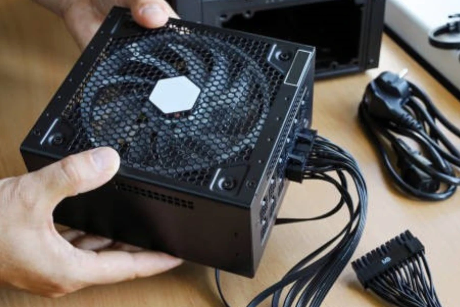 Man holding black power supply unit with power supply cables