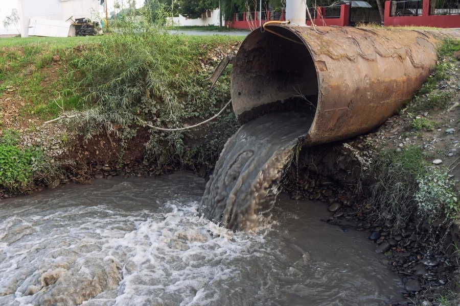 Загрязненная вода течет из труб в реку