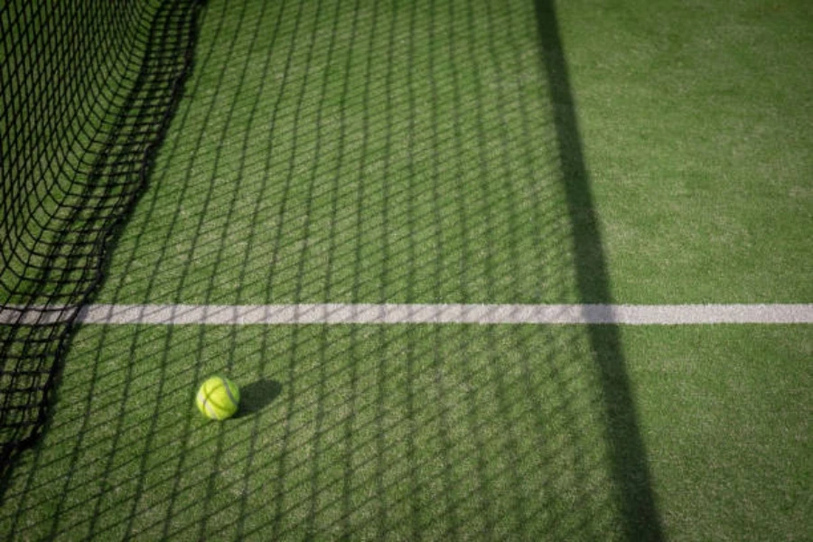 Bola tenis duduk dekat jaring di lapangan rumput buatan