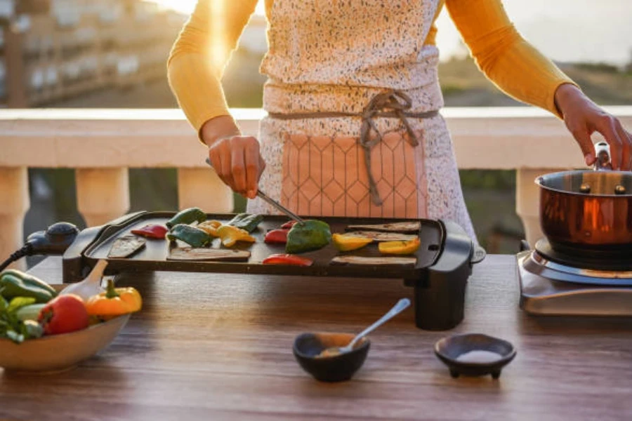 Frau auf der Terrasse mit elektrischem Tischgrill für Gemüse