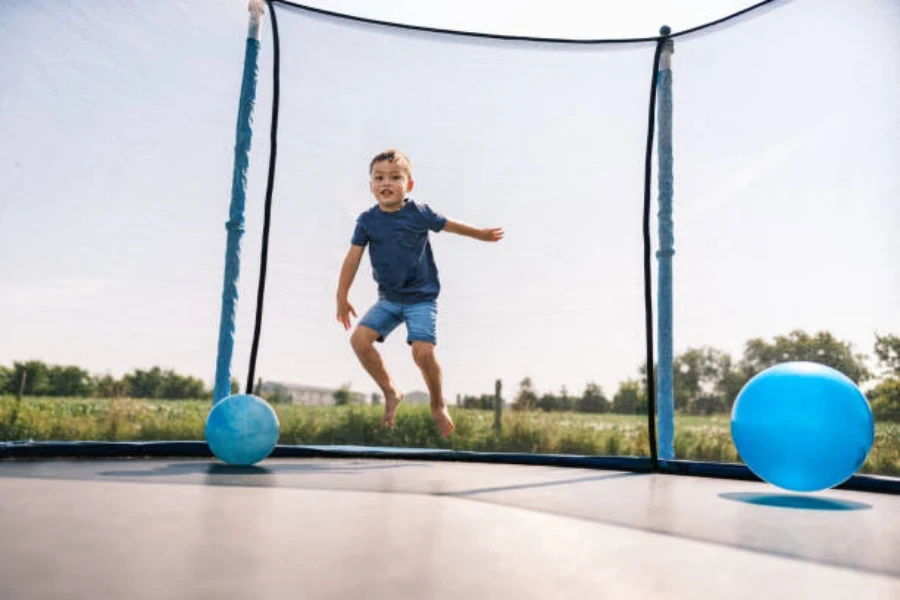 Kleiner Junge springt in einem geschlossenen Trampolin mit Bällen um ihn herum