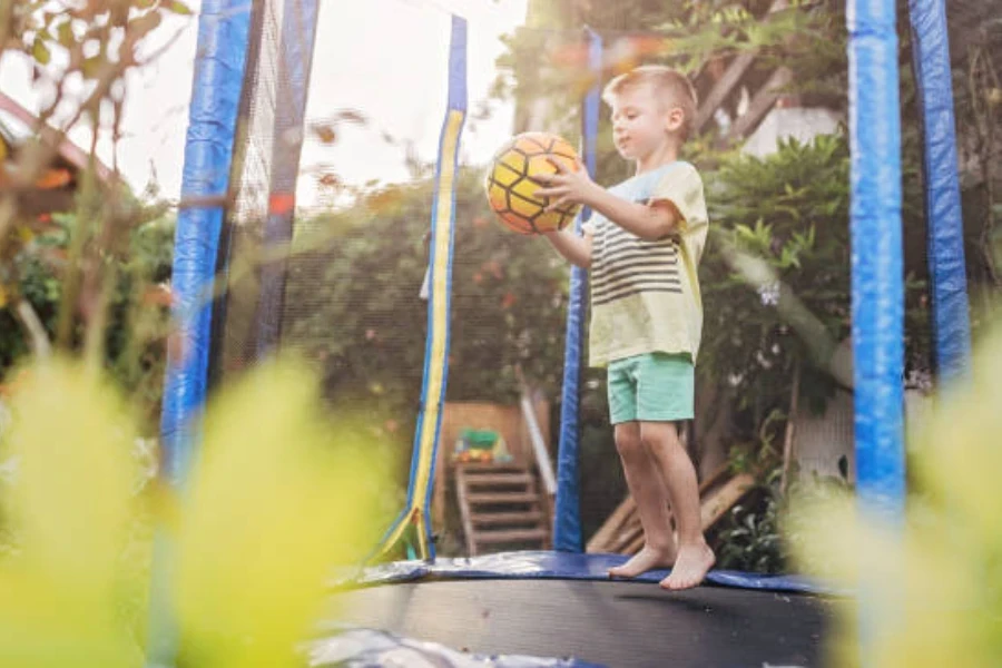 Menino pulando em um trampolim ao ar livre enquanto segura uma bola