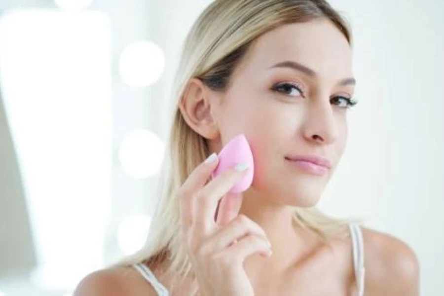 Jeune femme souriante en utilisant une éponge de maquillage