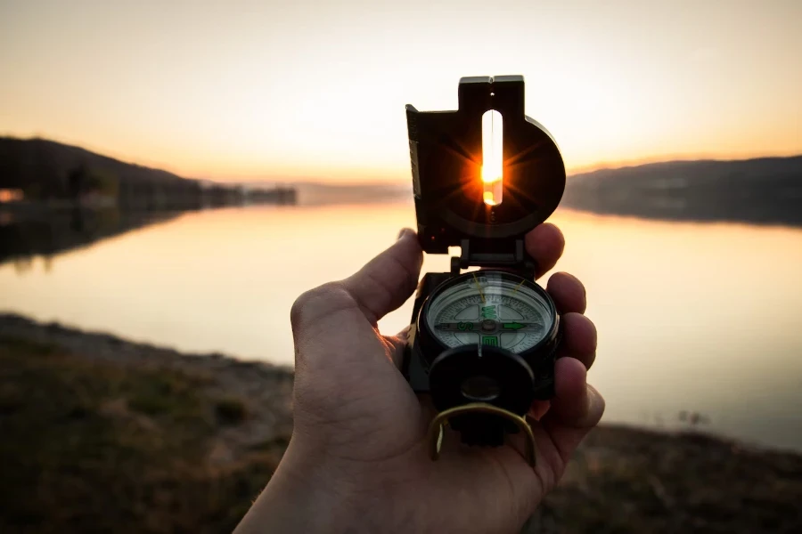 Mann hält Linsenkompass bei Sonnenuntergang neben einem kleinen See