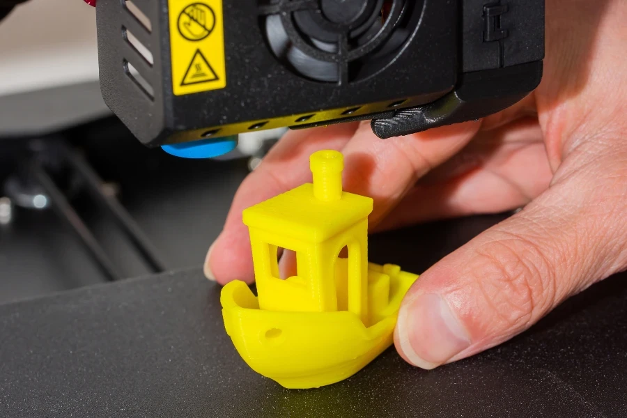 Seorang pria mengambil kapal mainan yang sudah jadi dari printer 3D