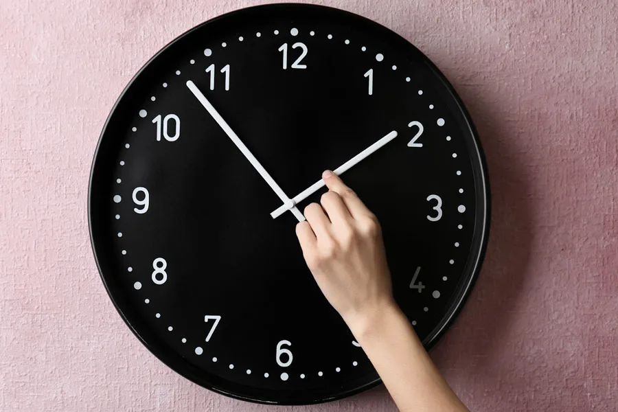 Un reloj de pared negro sobre un fondo rosa.