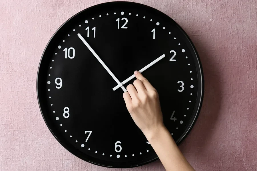 A black wall clock on a pink background