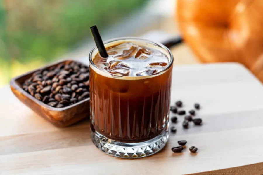 A glass of cold coffee with a few coffee beans lying around