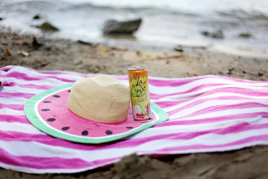 Un cappello e una lattina su un telo mare a righe