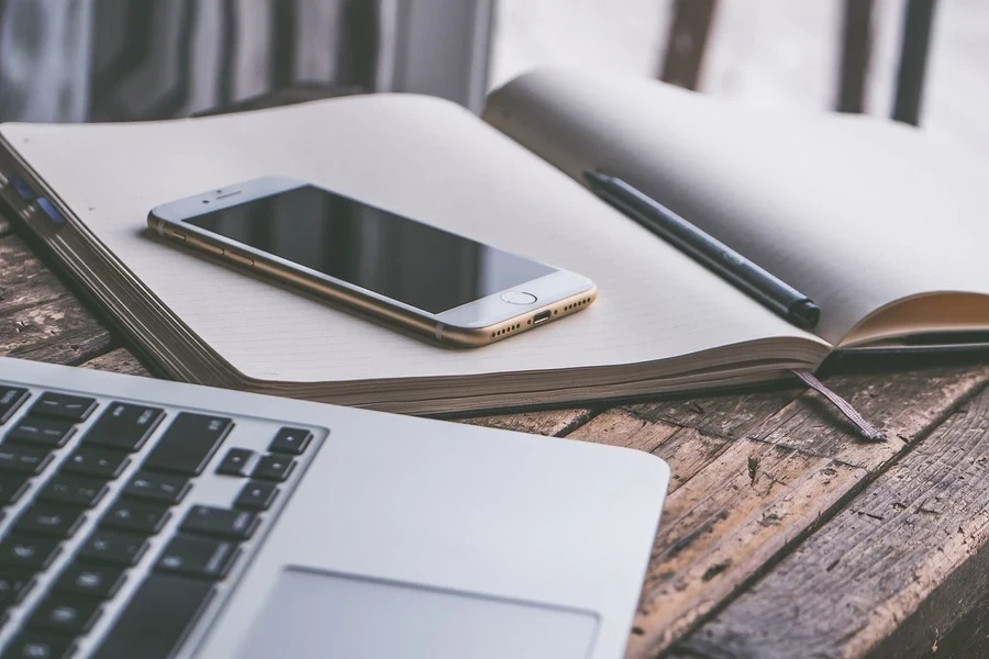 Una computadora portátil al lado de una libreta y un iPhone guardados en ella.