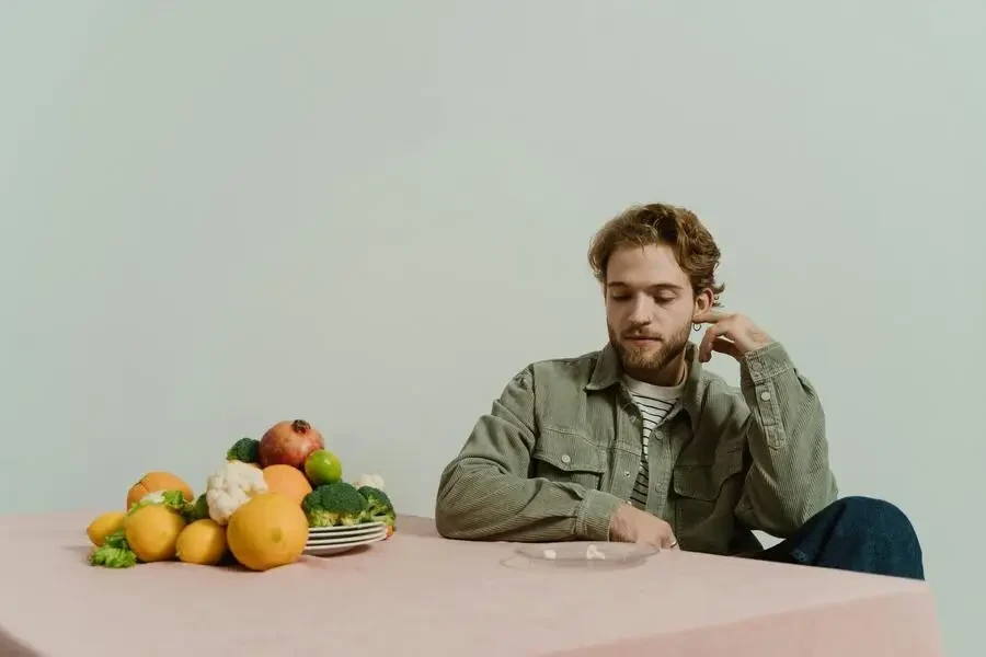 A man layering a green corduroy shirt with a white striped shirt looking at vegetables