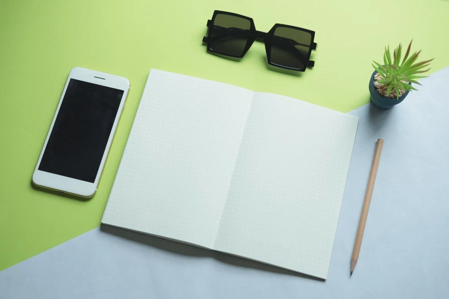 Un teléfono inteligente, una libreta, un lápiz y gafas de sol.