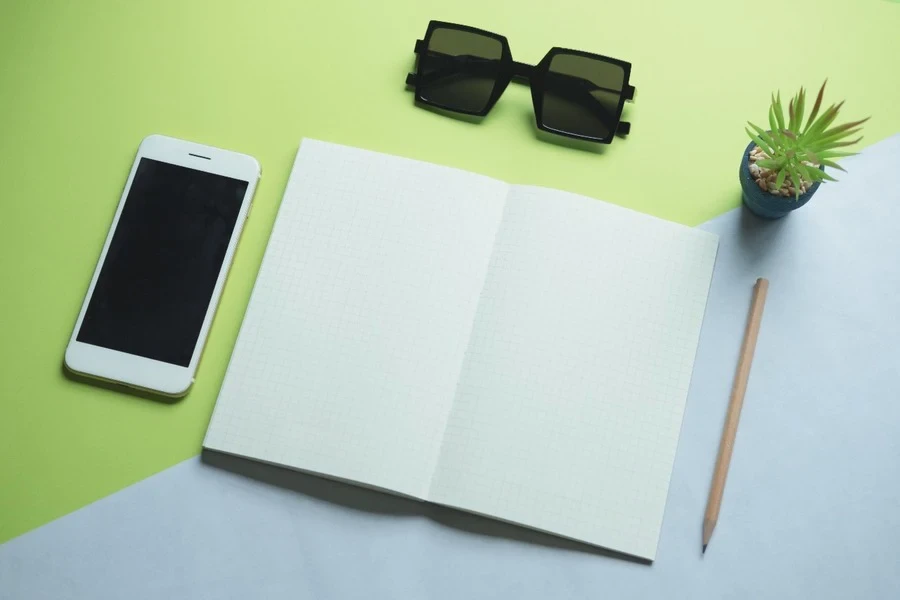 Ein Smartphone, ein Notizblock, ein Bleistift und eine Sonnenbrille