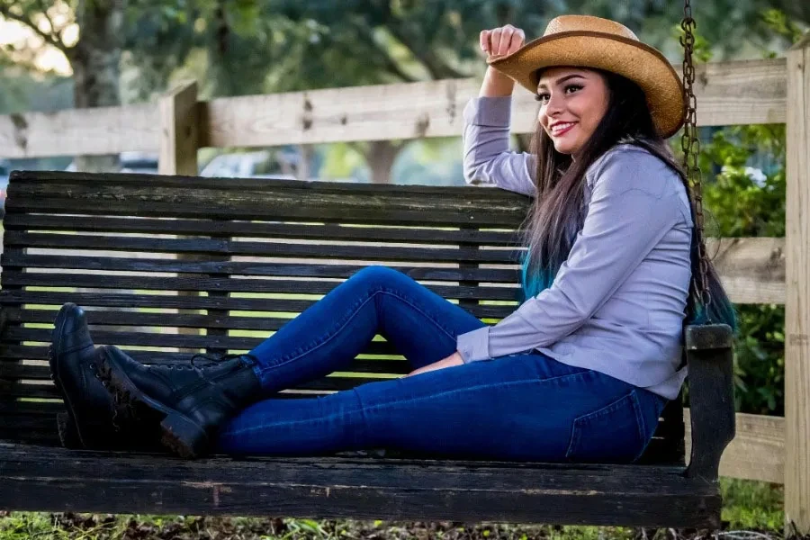 A woman sitting on a bench while wearing cowboy boots and hat