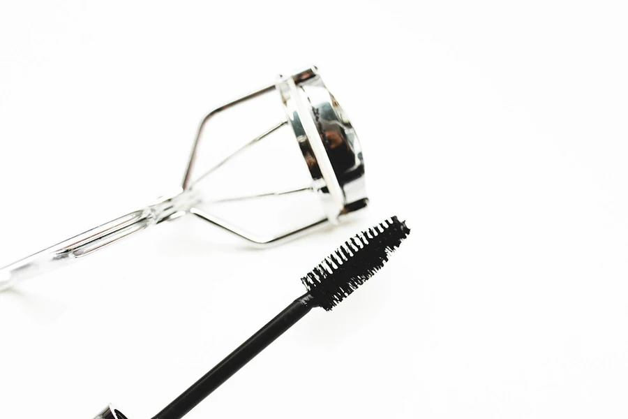 An eyelash curler next to a mascara brush