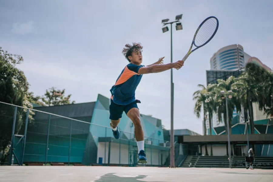 Boy swinging at ball in the air on hard tennis court