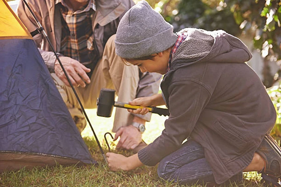 Boy using rubber camping mallet to drive a stake into the ground