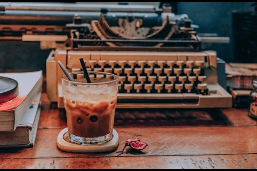 Kalter Kaffee im Glas, im Hintergrund eine Schreibmaschine