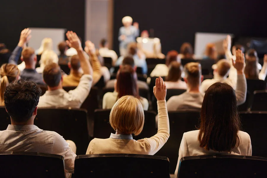 Multitud de personas levantando la mano en una reunión.