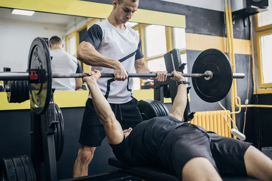 Gym buddy helping man with strength training on a bench