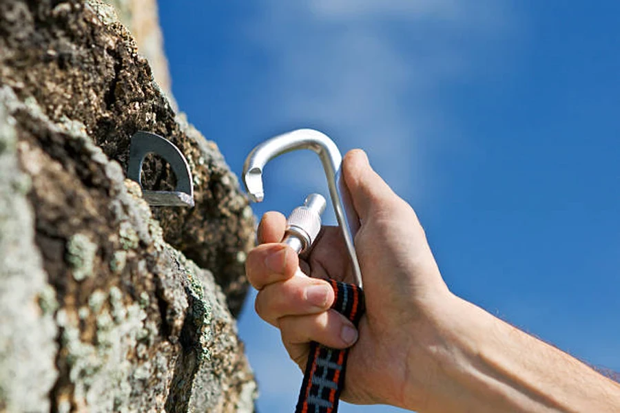 Hand attaching locking carabiner to hook in the rock