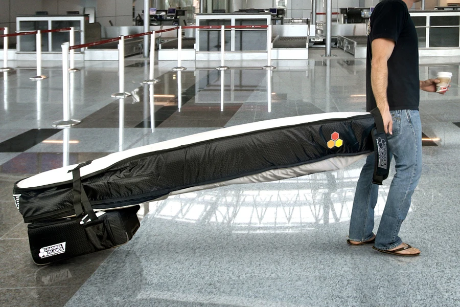 Мужчина тащит в аэропорту дорожную сумку с доской для серфинга