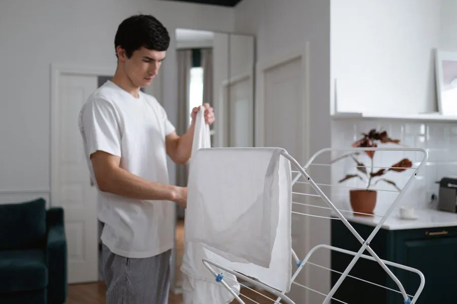 Mann trocknet Kleidung auf einem faltbaren Wäscheständer mit 3 Etagen