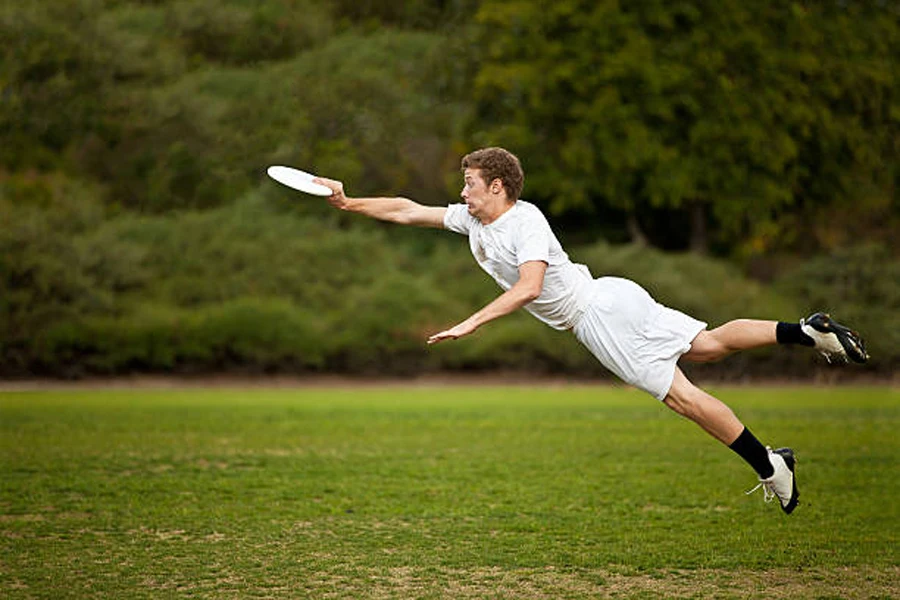 Hombre vestido de blanco saltando por el aire para atrapar un frisbee