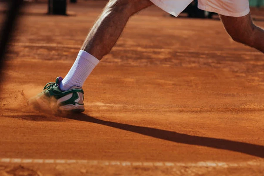 Man sliding on clay court wearing green lightweight tennis shoes