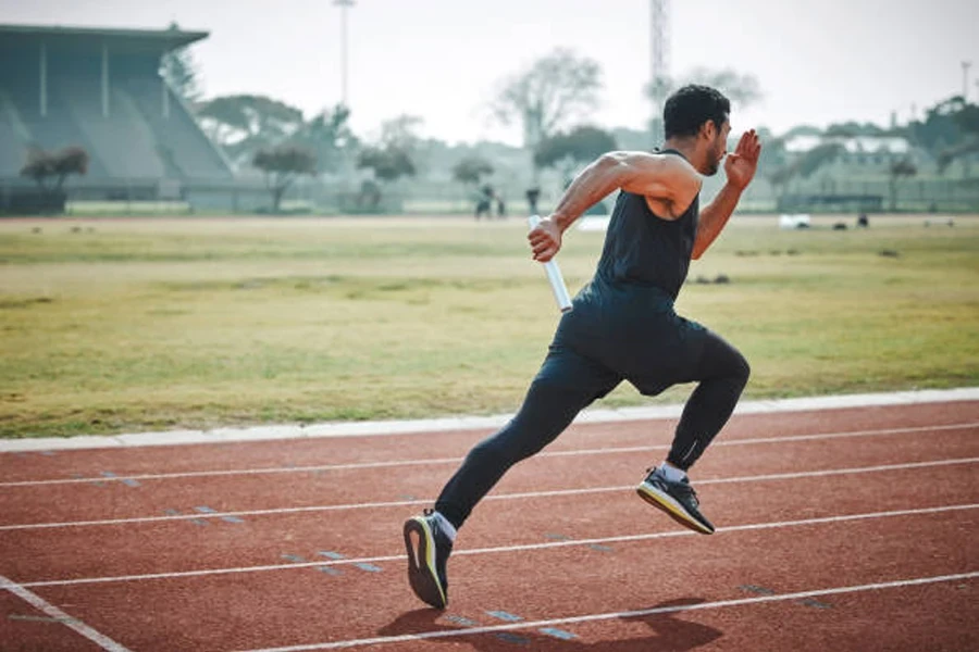 Homem correndo na pista enquanto segura um bastão de revezamento de metal