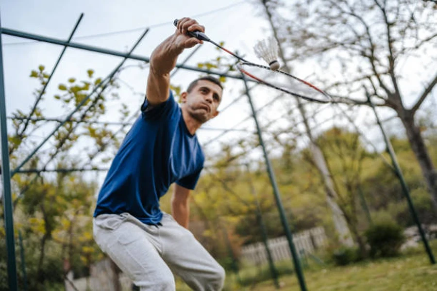 Man squatting to hit a white shuttlecock outdoors